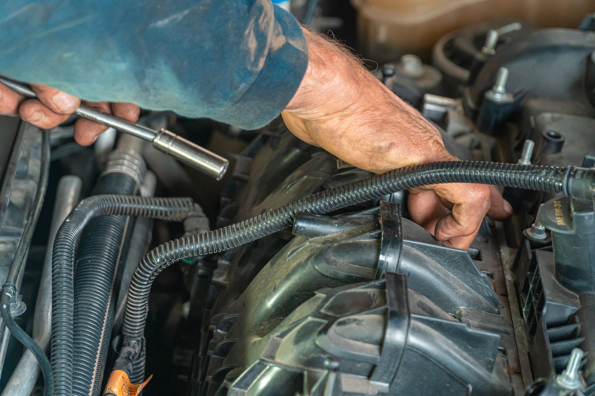 Hands using a socket wrench in an engine bay around the belt and accessory area