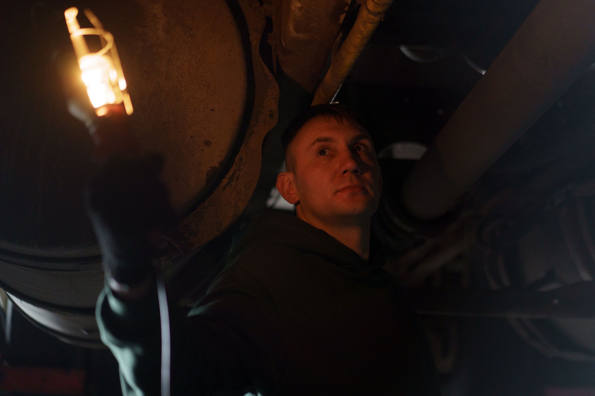 A mechanic holding a lit inspection lamp under a vehicle in near darkness — a stock photograph, not Reeves Mobile Mechanic's own work
